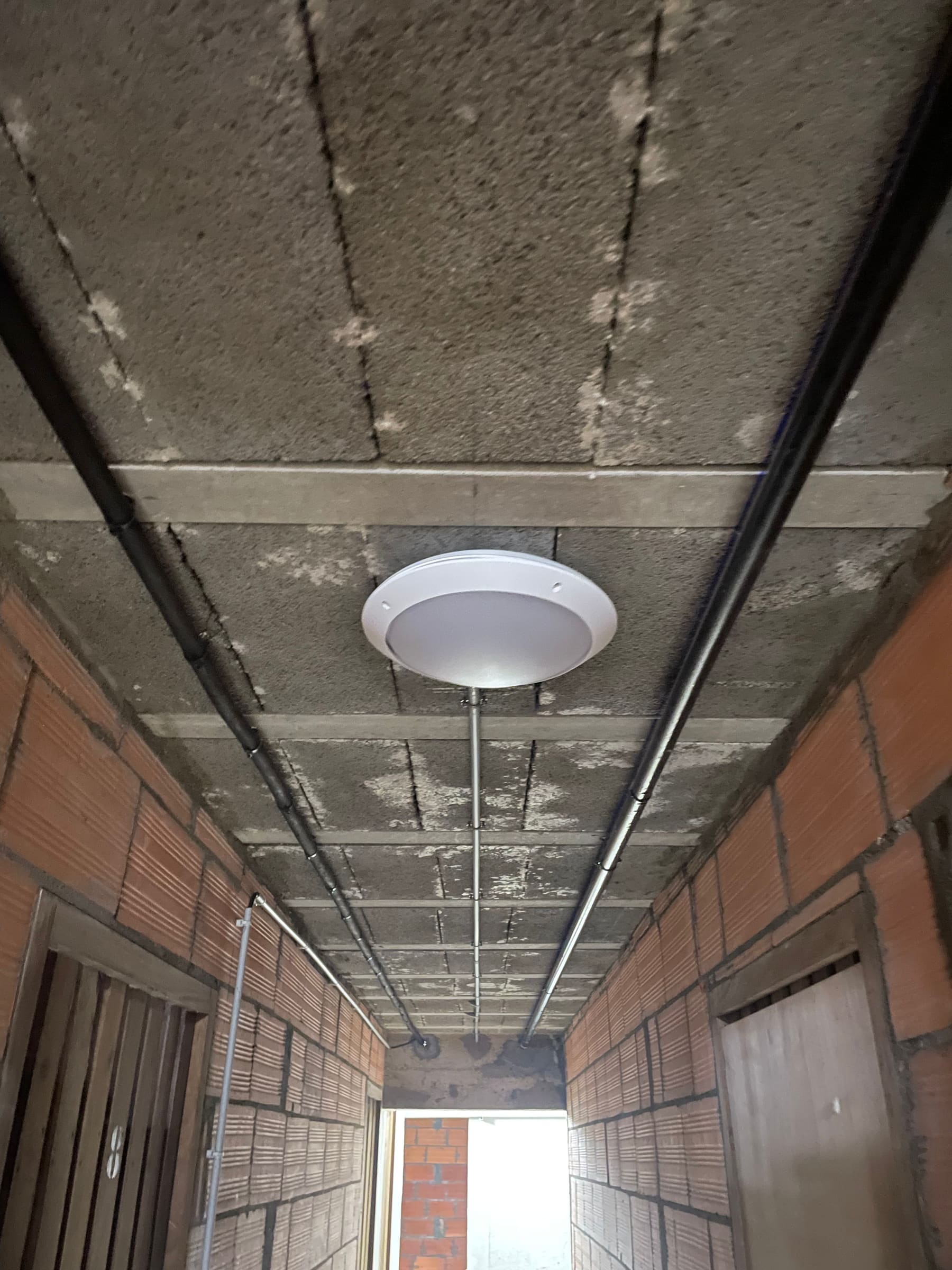 Hublot LED au plafond d’un couloir de caves, conduits électriques apparents