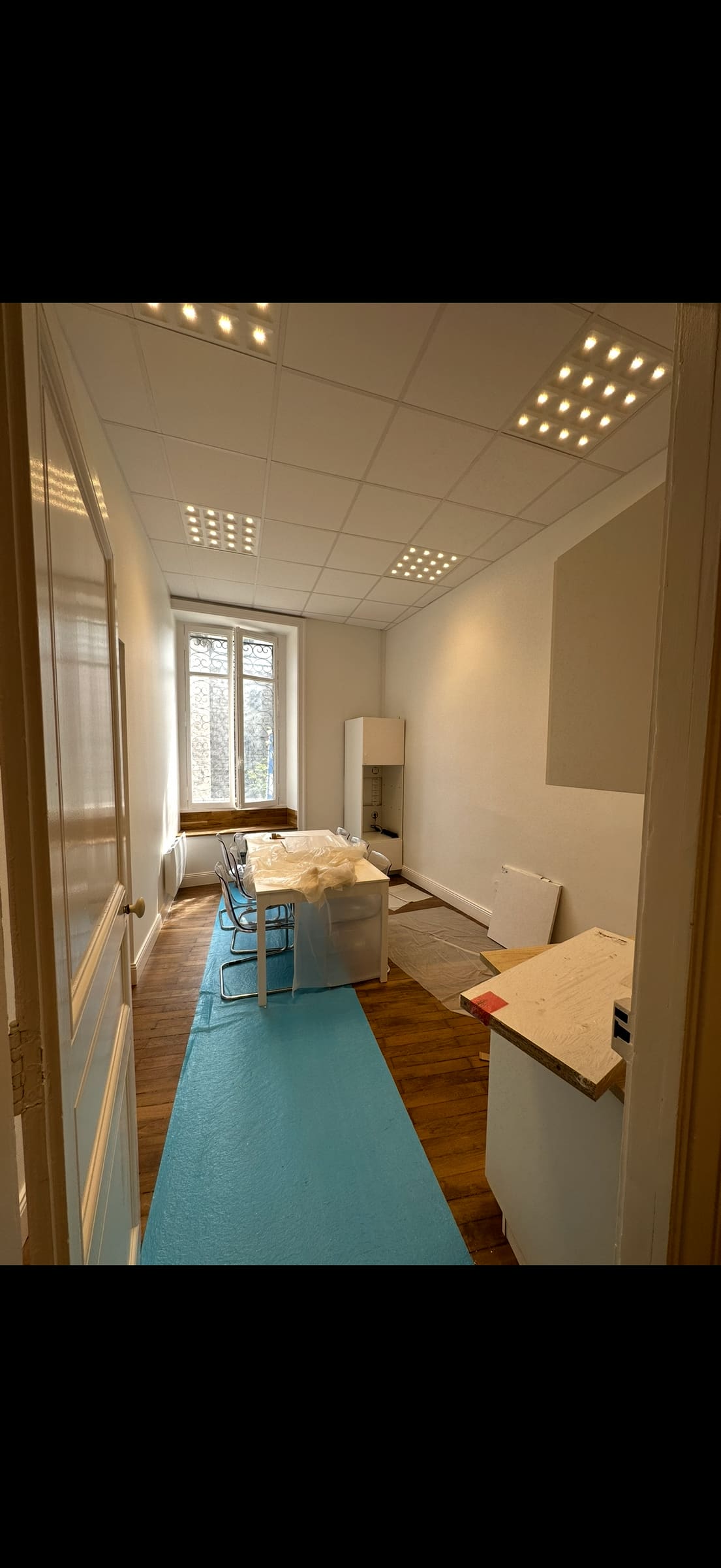 Bureau en rénovation, dalles LED allumées au plafond, sol protégé par une bâche