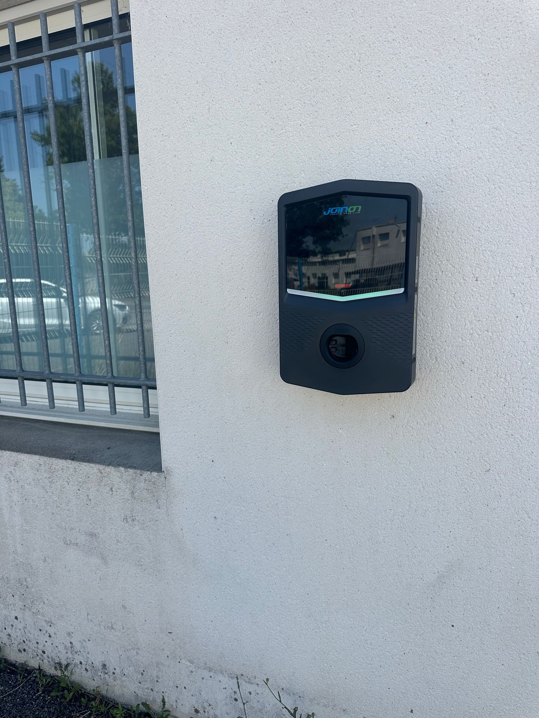 Borne de recharge murale fixée sur un mur crépi, près d’une fenêtre à barreaux