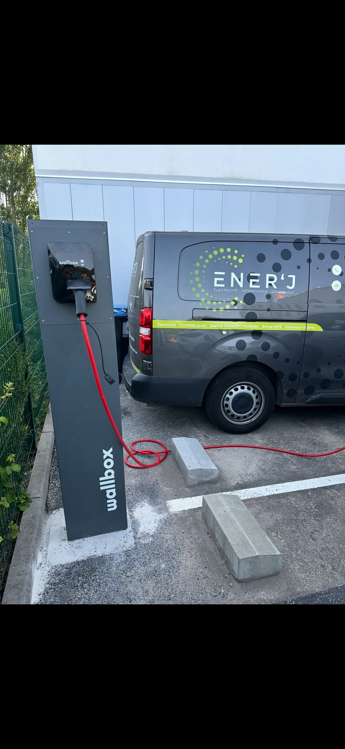 Borne Wallbox sur pied en charge, câble rouge branché à un utilitaire ENER'J