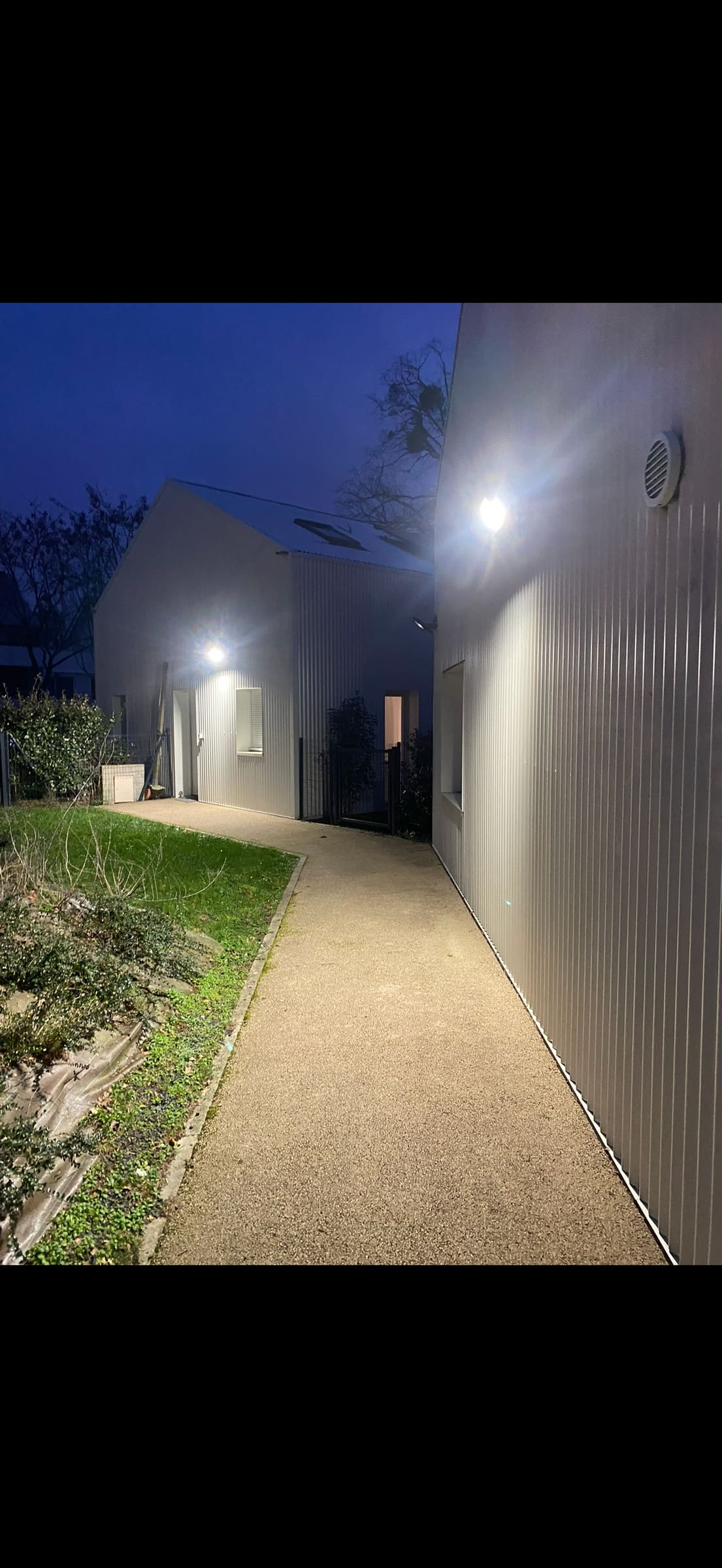 Allée extérieure éclairée la nuit par des projecteurs fixés en façade
