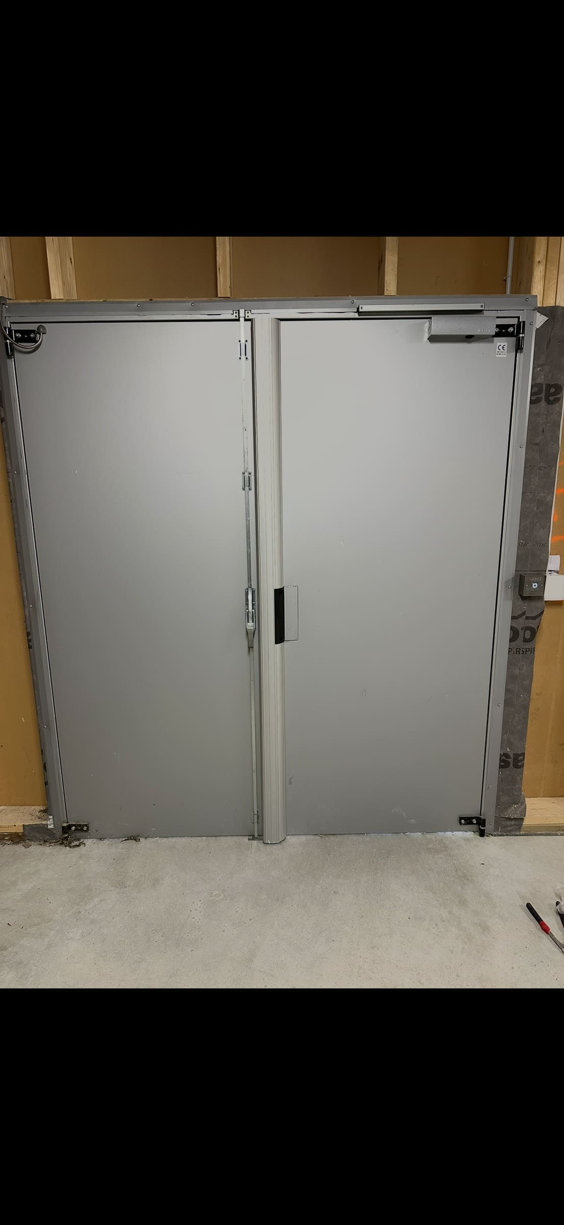 Double porte métallique d’un local commun, équipée d’un ferme-porte