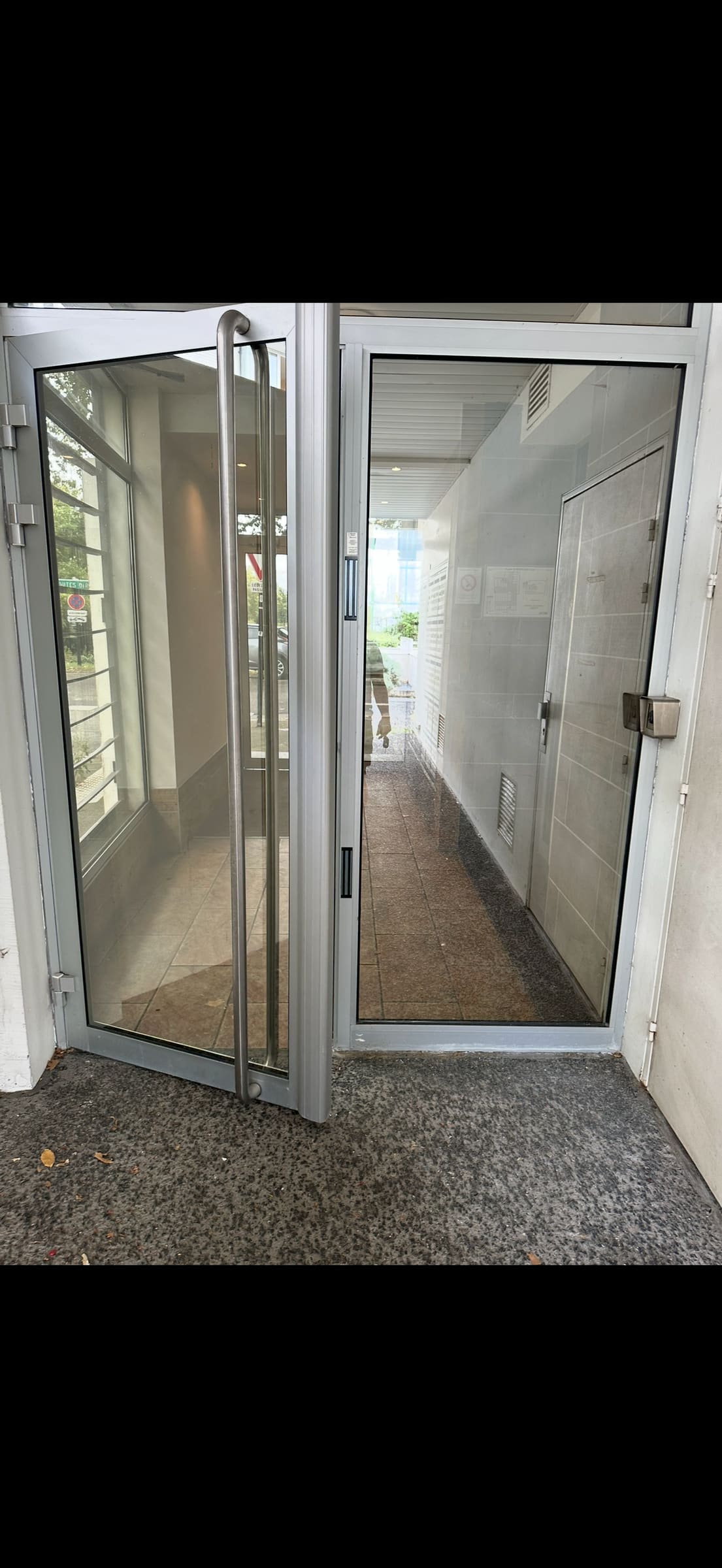 Porte vitrée d’un hall d’immeuble, deux vantaux ouverts sur le couloir