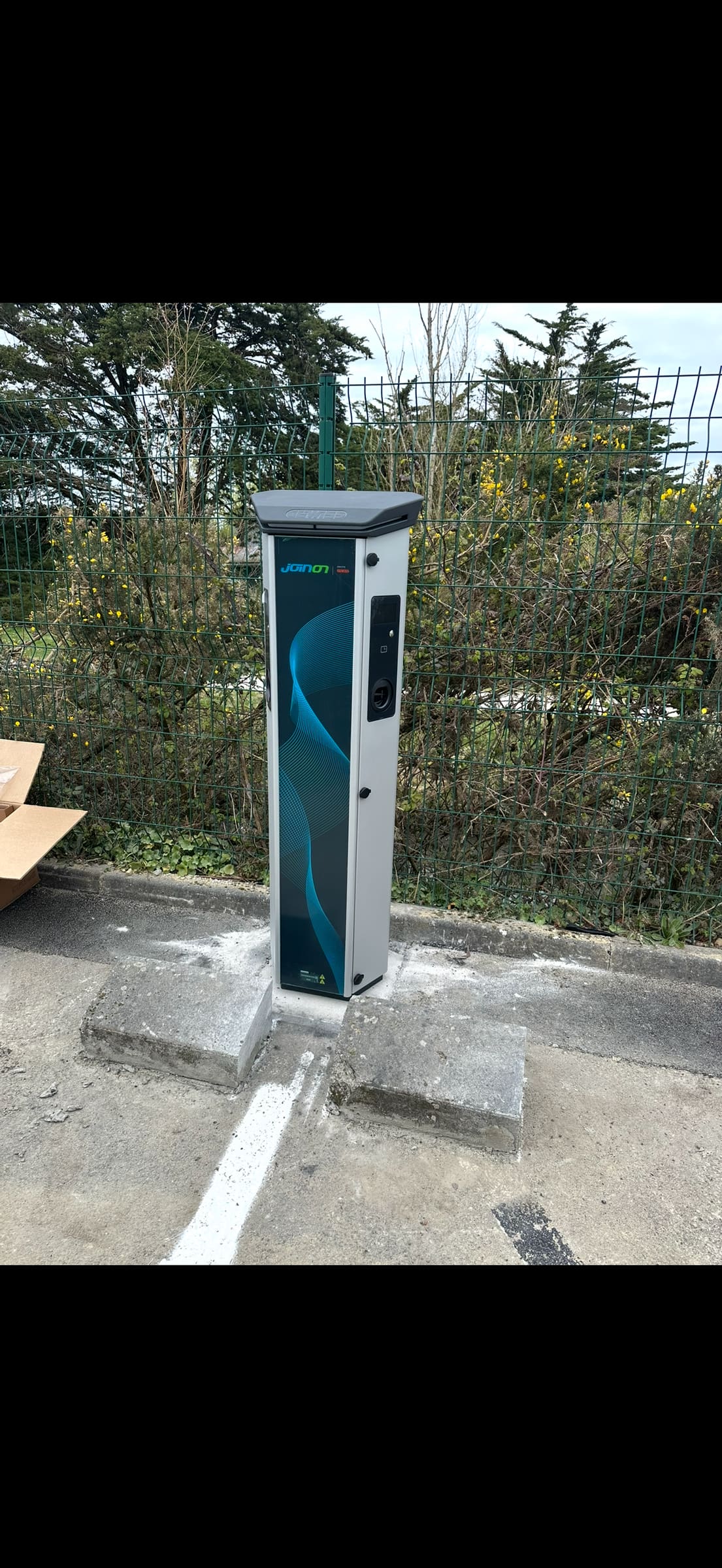 Borne de recharge sur pied posée en bout de place, sur un parking extérieur
