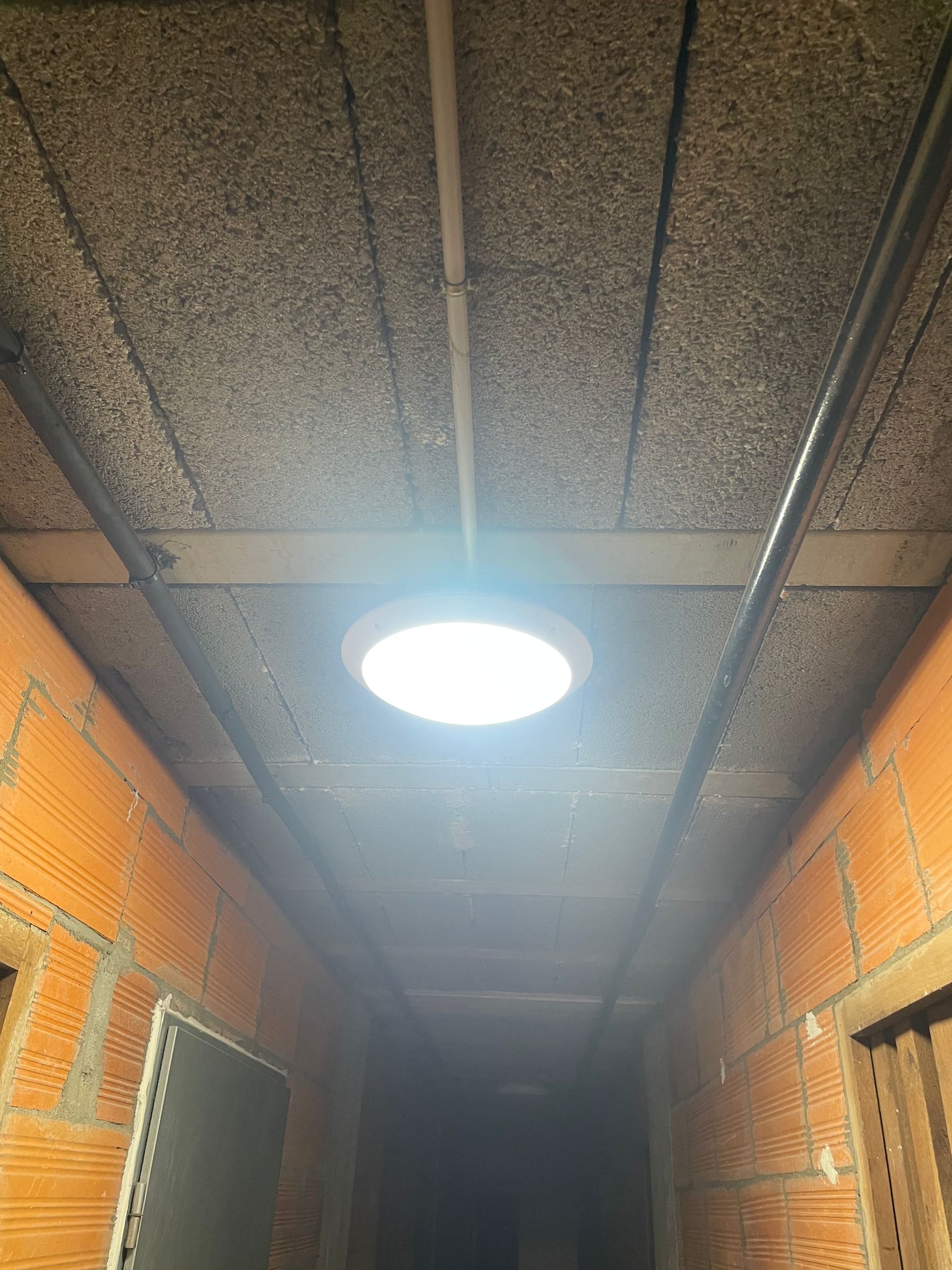 Couloir de caves éclairé par un hublot LED, conduits fixés au plafond